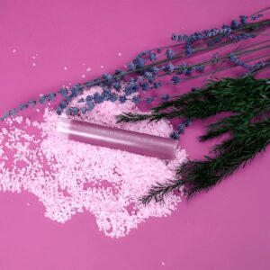 Lavender and rosemary herbs with pink bath salts and exfoliating tube on pink background, showcasing natural skincare, home spa products, and herbal wellness ingredients.
