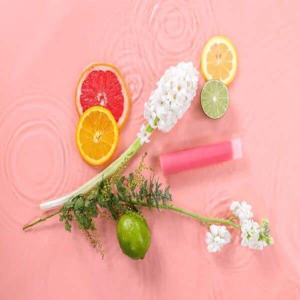 Vibrant citrus slices, a white hyacinth flower, a pink soap bar, and a green lime arranged on a soft pink water background, highlighting freshness and natural ingredients for skincare or wellness products.