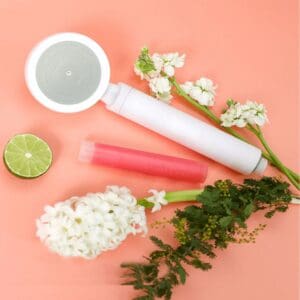 Replaceable water filter cartridge with flowers and citrus for natural water purification, showcasing portable filtration device and fresh ingredients on a soft pink background.