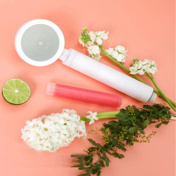 Replaceable water filter cartridge with flowers and citrus for natural water purification, showcasing portable filtration device and fresh ingredients on a soft pink background.