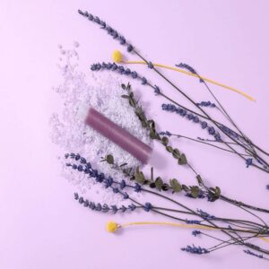 Lavender and yellow billy button flowers with a purple bath bomb surrounded by bath salts on a pastel purple background, highlighting natural bath products and floral spa essentials.