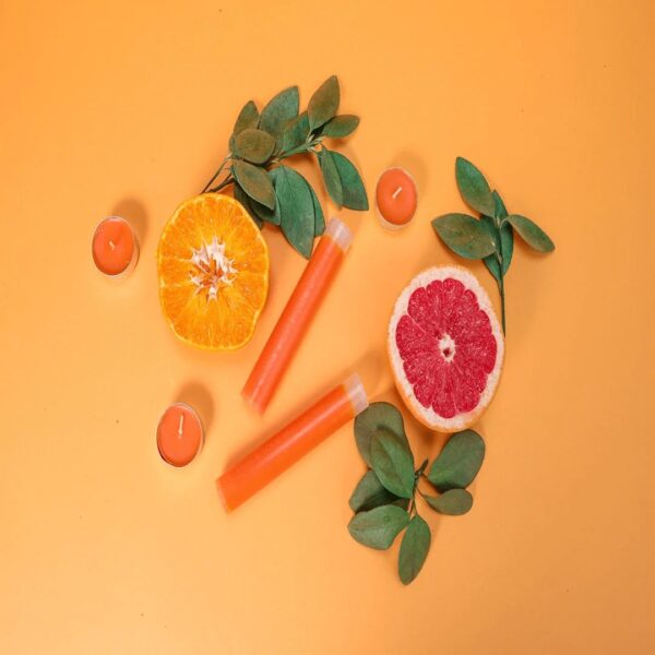 Vibrant citrus slices with candles and green leaves on a warm orange background for fresh scent and air purification.