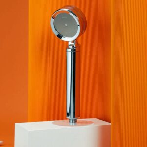 Modern handheld showerhead with chrome finish against orange textured background.