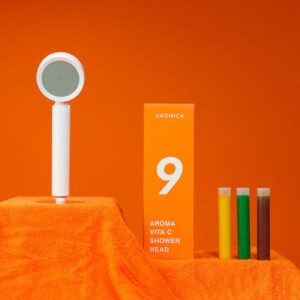 Aroma Vita C Shower Head with colorful test tubes, vibrant orange background, modern design, and packaging, highlighting air and water purification for healthy skincare and shower experience.