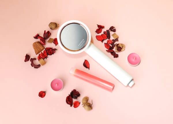 Aromatherapy diffuser with dried flower petals, candles, and essential oil bottle on a pink background, emphasizing home fragrance and relaxation products.