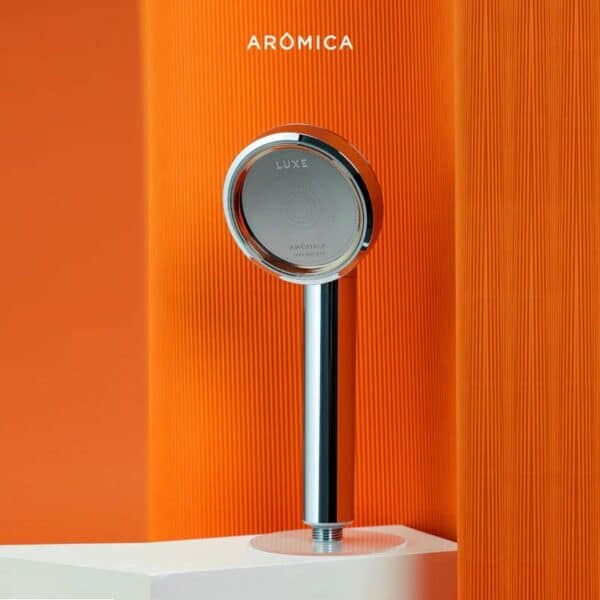 Sleek modern shower head with chrome finish against vibrant orange textured background for bathroom decor and plumbing fixtures.
